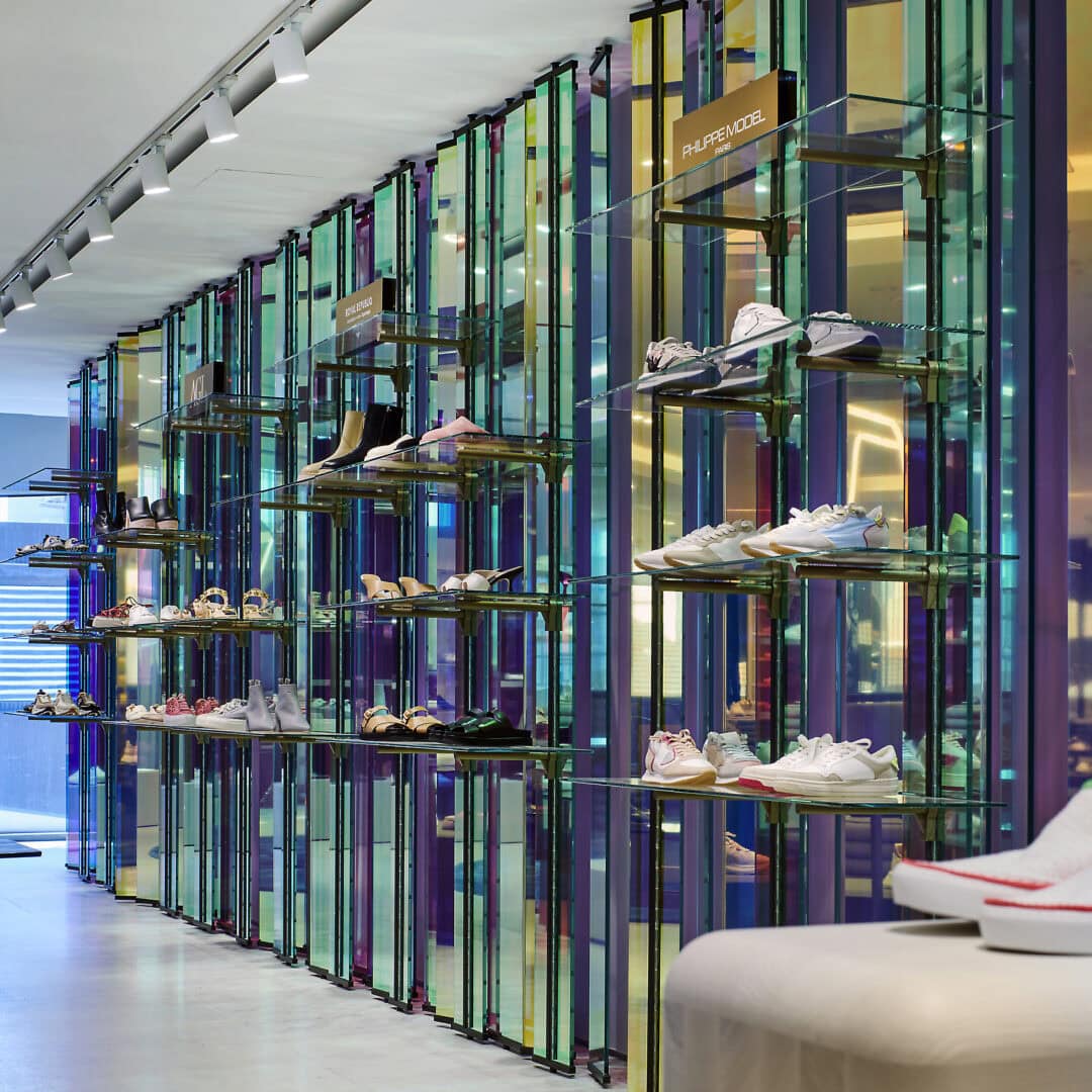 Moderne Schuhregale mit transparenten, bunten Glaswänden und Beleuchtung in einem Laden, der von KRAISS ausgestattet wurde.