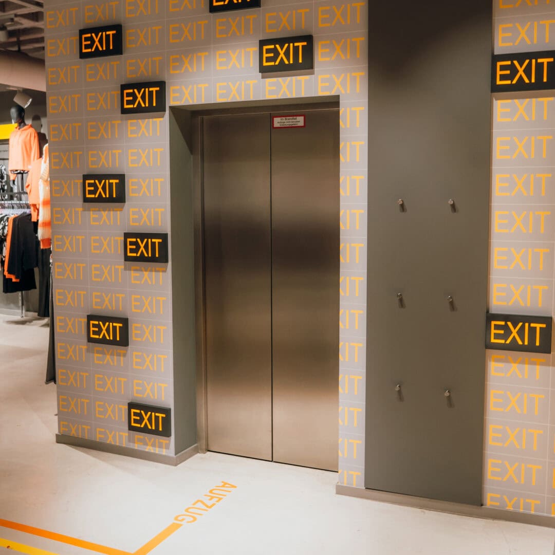 Modernes Shopfitting mit beleuchteten EXIT-Schildern und Fluchtwegmarkierungen an der Wand und auf dem Boden.