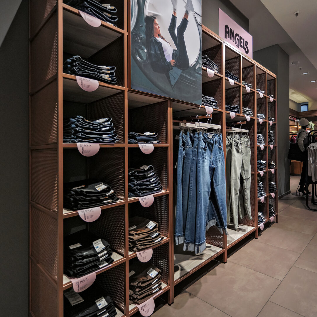 Modische Kleidung und Accessoires im von KRAISS gebauten Shop-in-Shop, präsentiert auf stilvollen Regalen und Kleiderstangen, ideal für trendbewusste Kunden.