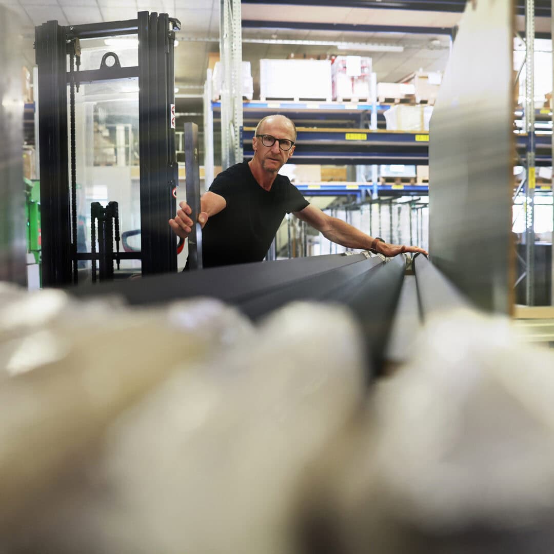 Mitarbeiter in einer Fertigungshalle bei KRAISS, umgeben von Regalen und Produktionsmaterialien, mit gut ausgeleuchteten Arbeitsbereichen.