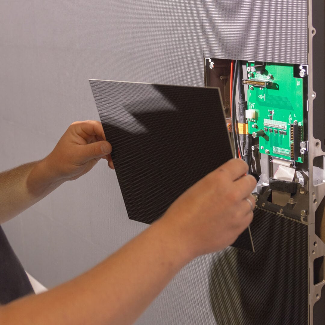Mitarbeiter installiert digitale Anzeigetafel in einem Laden, zeigt elektronische Komponenten und Verkabelung.