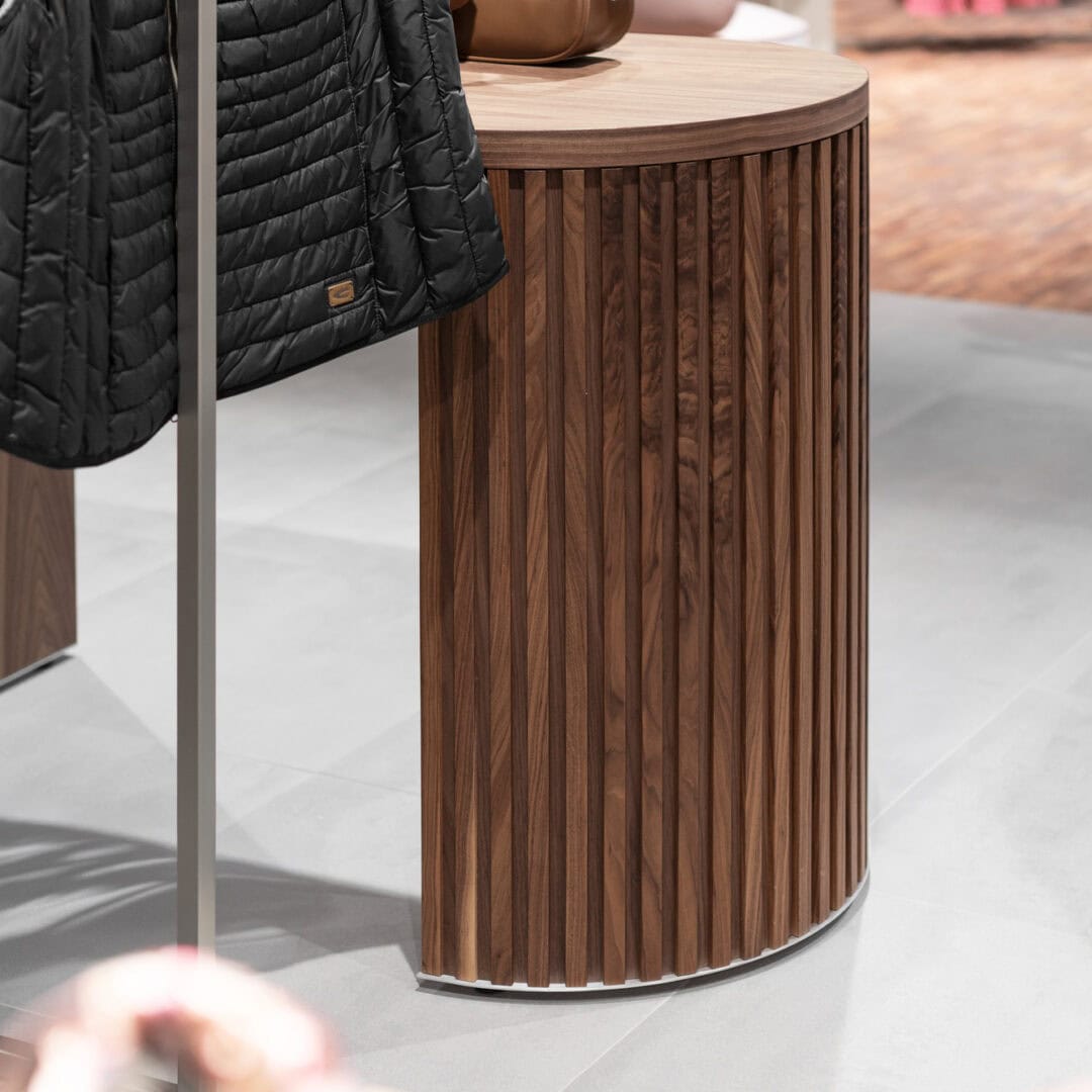 Eleganter Tisch aus Holz mit runden Design, ideal für Modeboutiquen und Geschäfte, um Handtaschen stilvoll zu präsentieren und Ordnung zu schaffen.