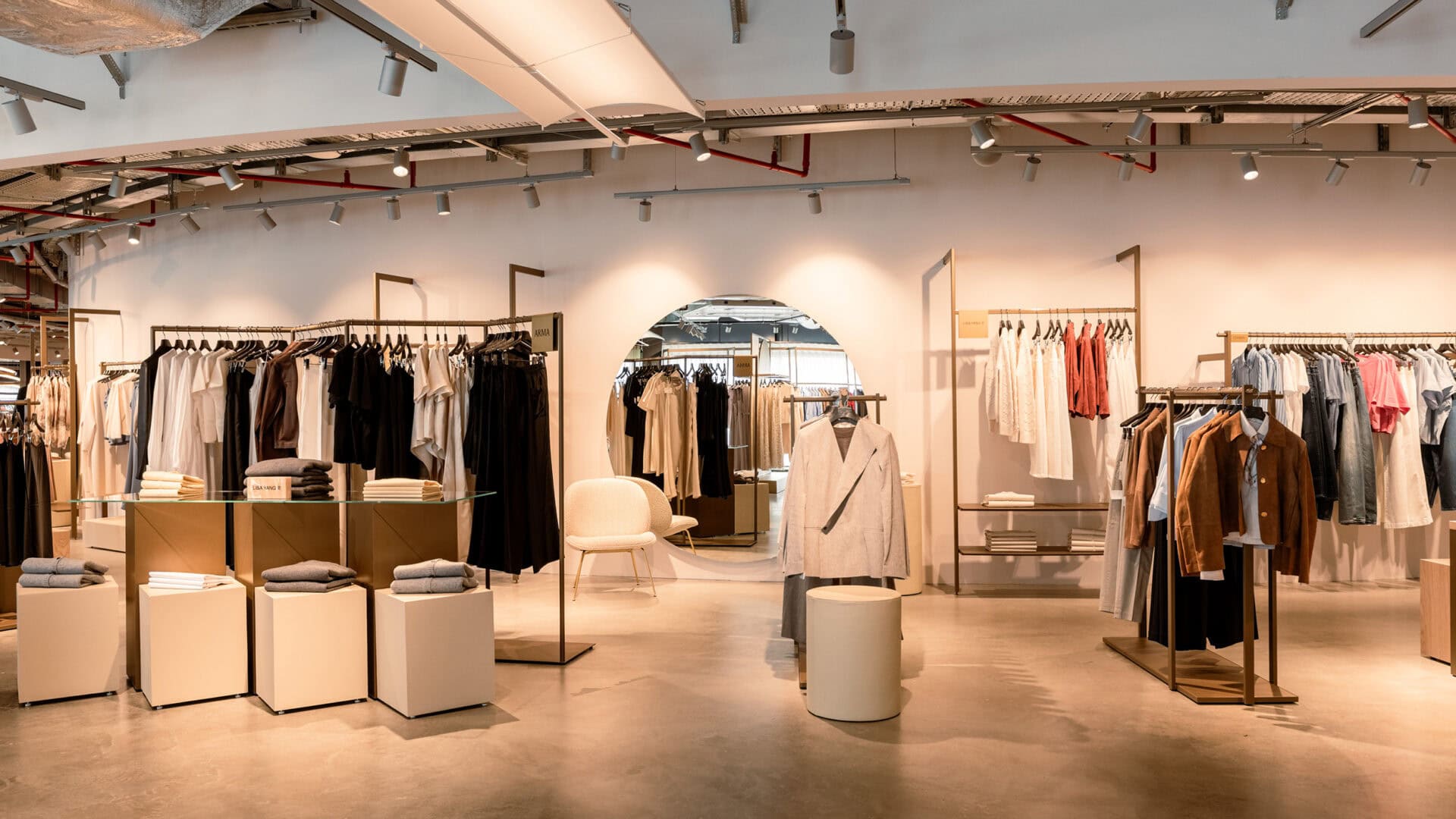 Moderne Modeboutique mit Kleidung auf Kleiderstangen und Sitzgelegenheiten, helles und einladendes Einkaufserlebnis bei KRAISS.