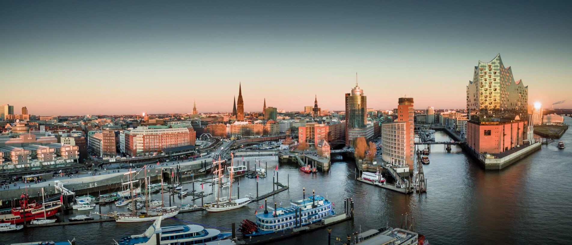Panoramablick auf Hamburg mit Hafen, Elbphilharmonie und Hafenkränen bei Sonnenuntergang, ideal für Ladenbau- und Innenausbau-Projekte.