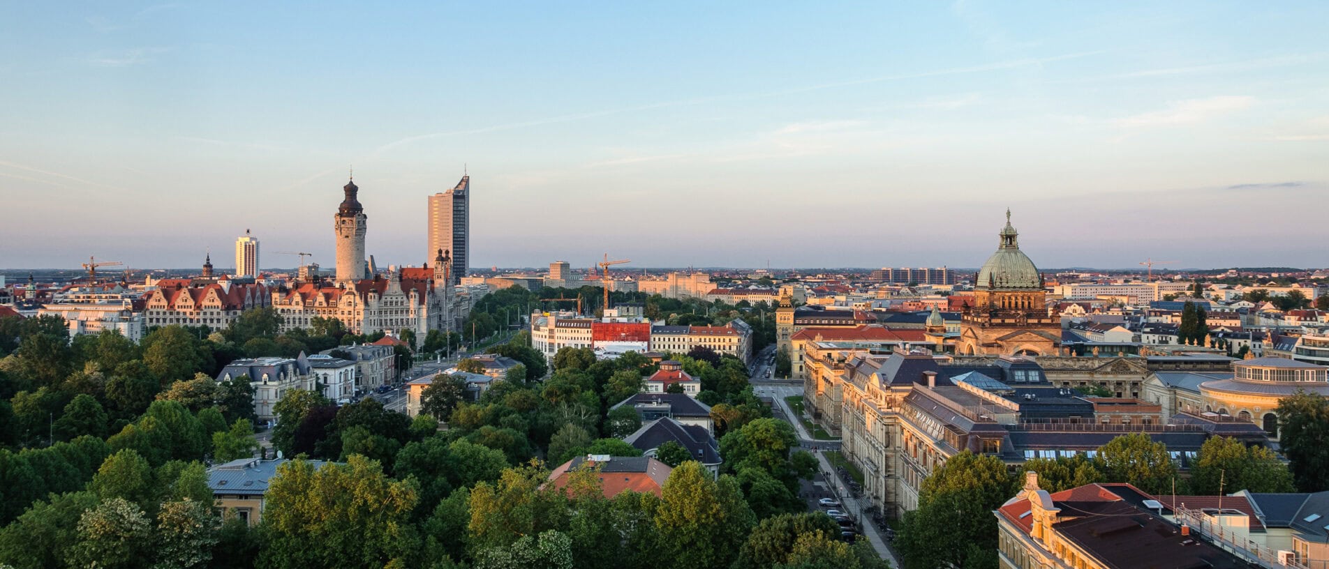 Panorama von Leipzig mit historischen Gebäuden, Türmen und grünen Parks bei Sonnenuntergang, ideal für Ladenbau und Innenarchitektur.