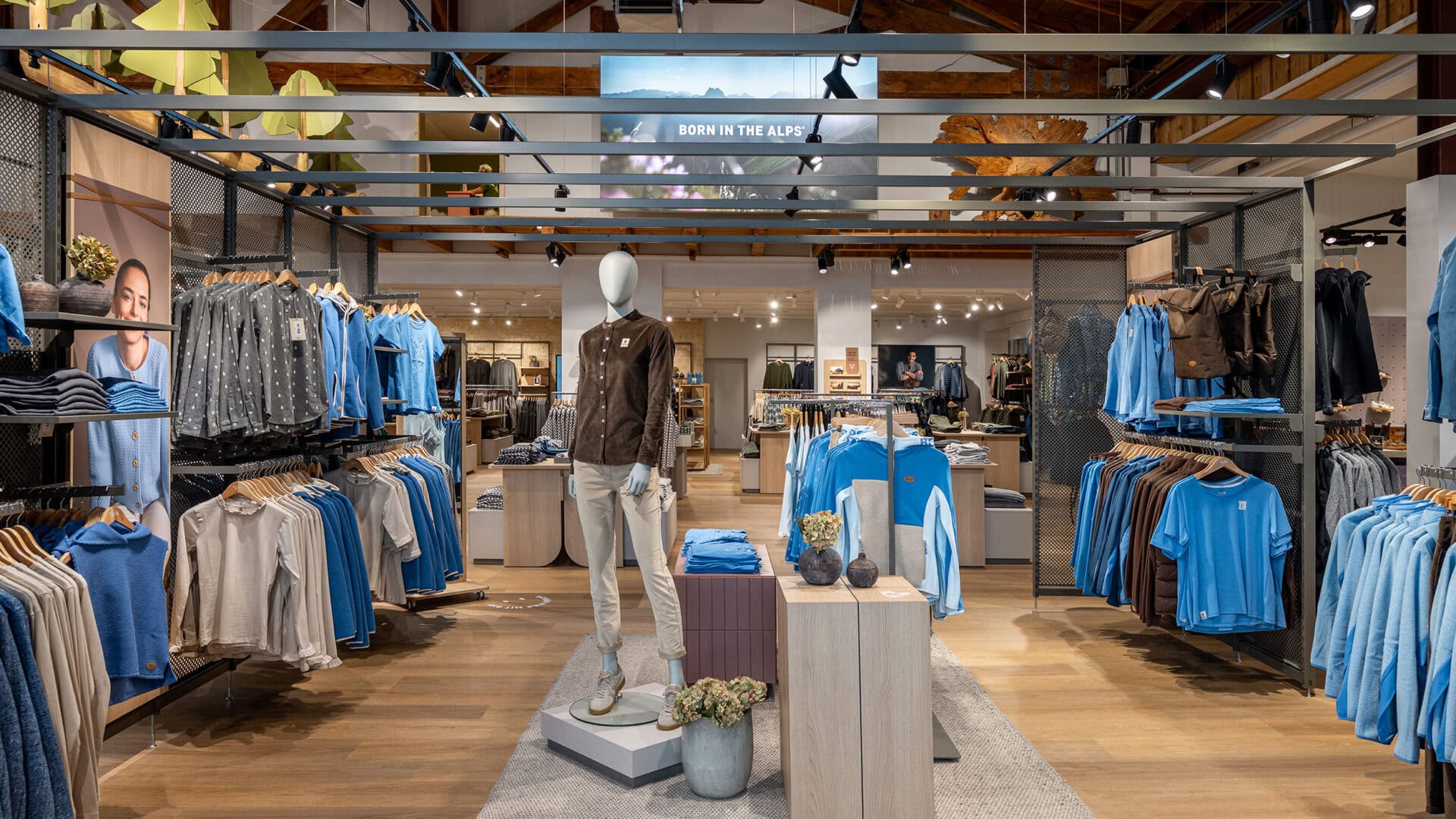 Innenansicht eines Modegeschäfts mit blauer Kleidung auf Kleiderstangen und einem Manne-Display in der Mitte.