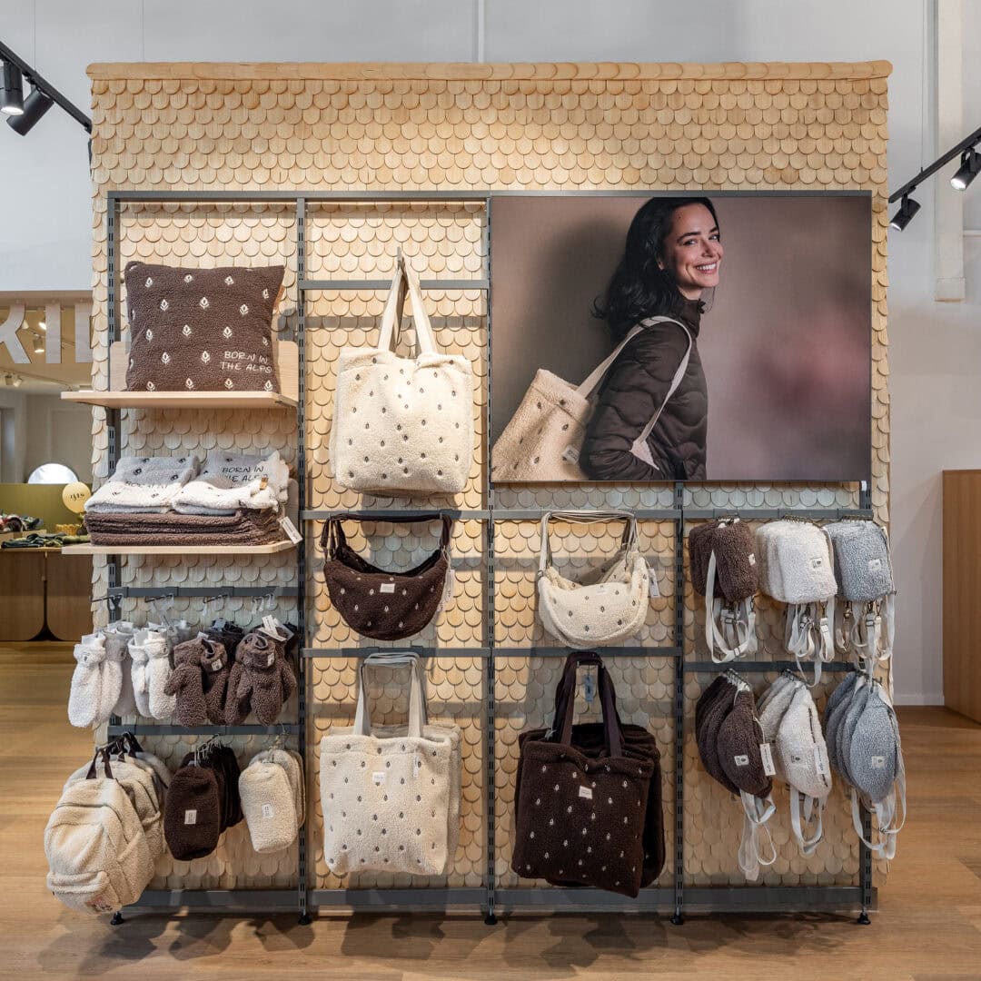 Verkaufstheke mit Handtaschen, Rucksäcken und Kissen, großes Bild einer lachenden Frau im Hintergrund.