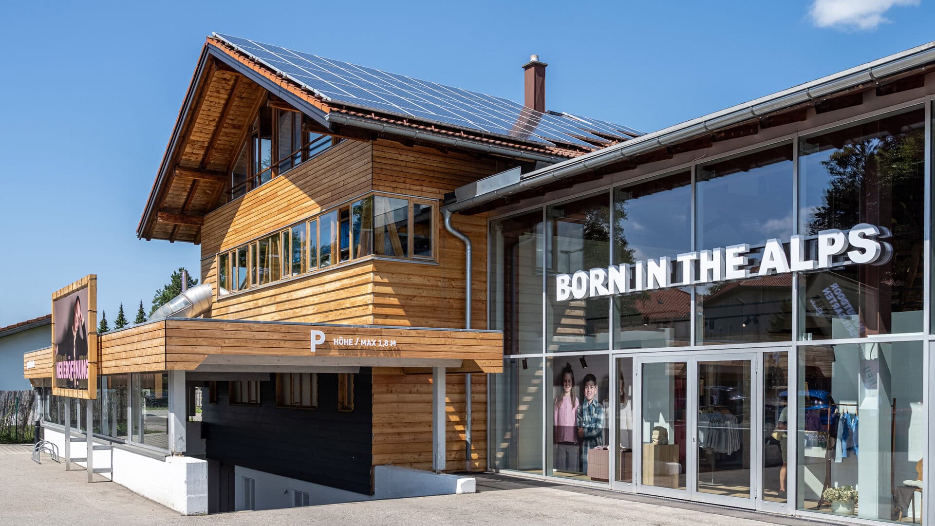 Modernes Gebäude mit Holzfassade, Solarzellen auf dem Dach und großem Glasfenster mit Aufschrift 