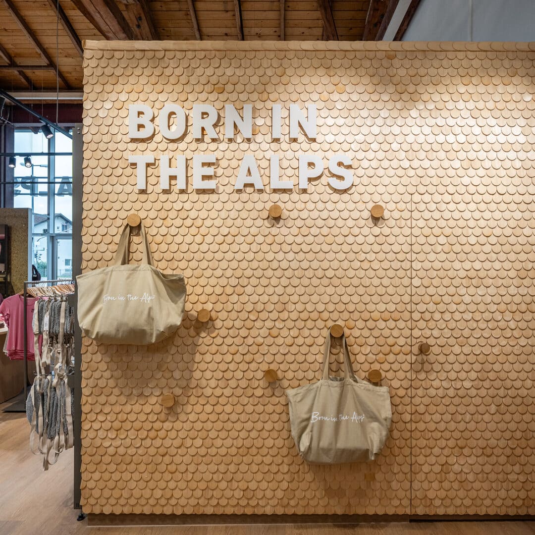 Wanddekoration mit Text 'BORN IN THE ALPS' und zwei Taschen in einem Geschäft.